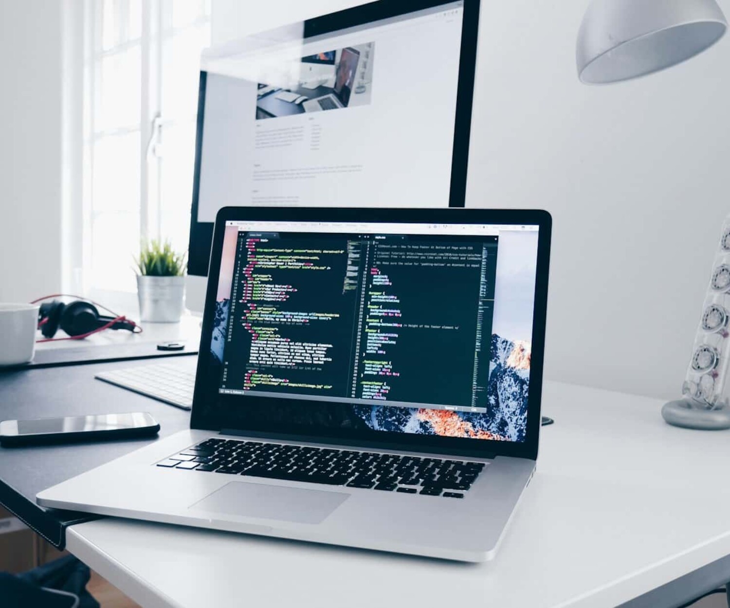 A MacBook with lines of code on its screen on a busy desk